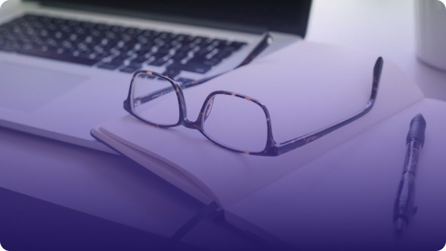 Glasses and notebook resting on an open laptop