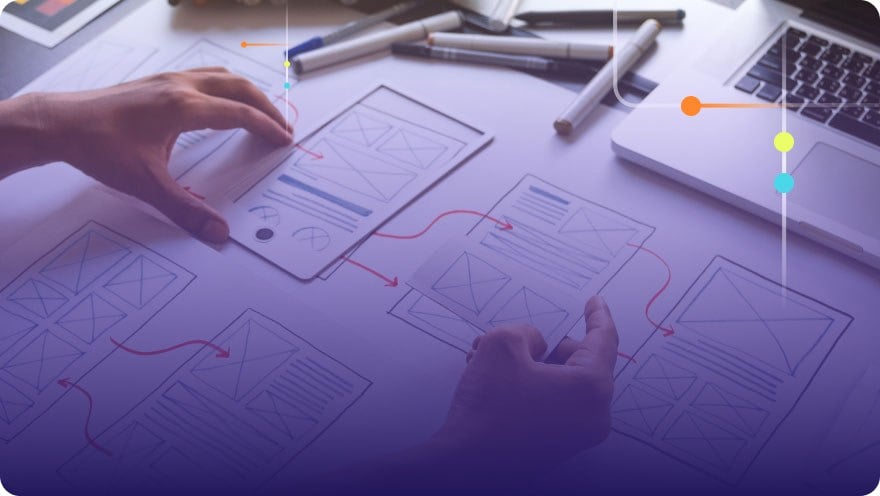 A product designer lays out paper wireframe cut-outs on a desk with hand-drawn arrows, showing a proposed user flow